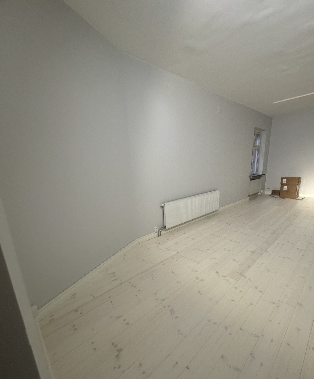 Ljust nymålat rum med ljusgrå väggar, vita trägolv och högt fönster en fräsch bas för vidare inredning efter renovering